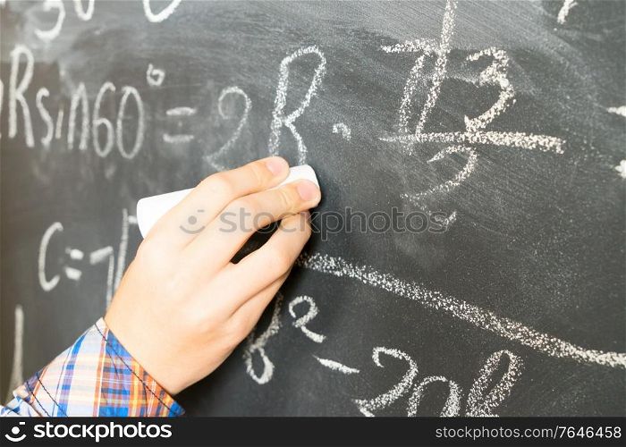 Hand with chalk writting math formulas on black board close up. Hand writting on black board