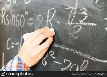 Hand with chalk writting math formulas on black board close up. Hand writting on black board