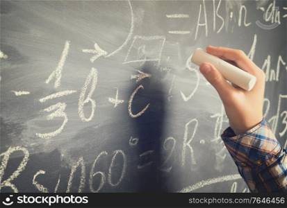 Hand with chalk writting on math formulas black board, retro toned. Hand writting on black board