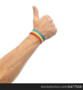 hand with gay pride rainbow wristband shows thumb. lgbt, same-sex relationships and homosexual concept - close up of male hand wearing gay pride awareness wristband showing thumbs up