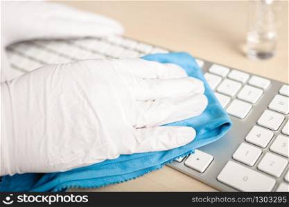 Hand with gloves cleaning a keyboard with disinfectant. COVID-19 Coronavirus outbreak contamination prevention concept