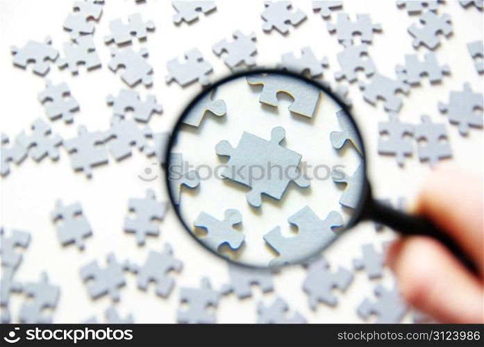 Hand with magnifying glass and puzzle isolated on white background