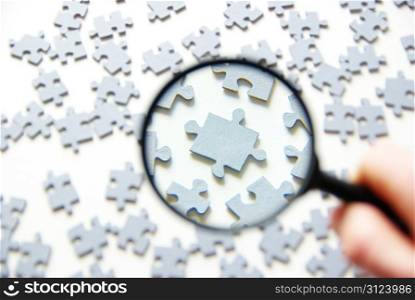 Hand with magnifying glass and puzzle isolated on white background