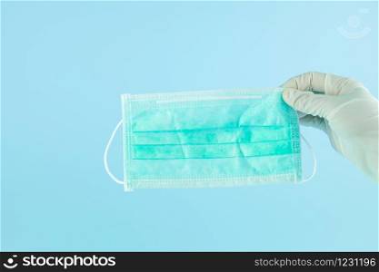 Hand with medical glove holding Protective face mask on blue background, against Novel coronavirus (2019-nCoV) or Wuhan coronavirus and Influenza. Antiseptic, Hygiene and Healthcare concept
