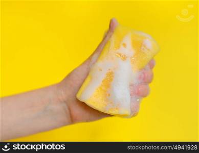 Hand with sponge with foam on yellow background