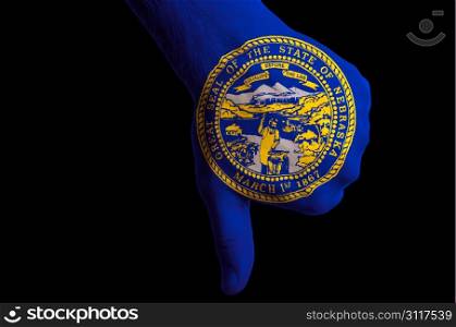 Hand with thumbs down gesture in colored american state of nebraska flag as symbol of negative political, cultural, social management of state