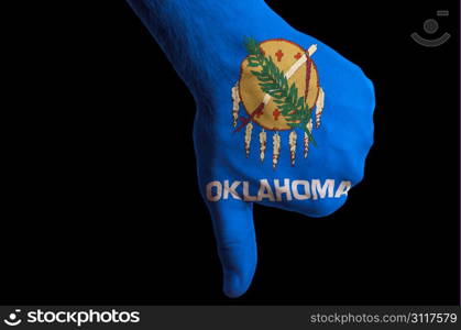 Hand with thumbs down gesture in colored american state of oklahoma flag as symbol of negative political, cultural, social management of state