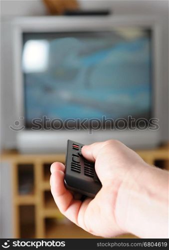 Hand with TV remote controller change the TV channel.