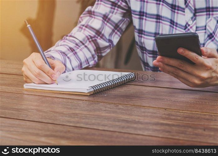 Hand woman holding phone and writing notebook on wood table with cup coffee.