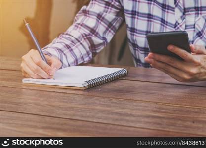 Hand woman holding phone and writing notebook on wood table with cup coffee.
