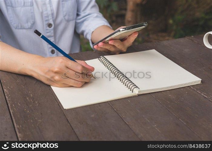 Hand woman write notebook and holding phone on wood table.