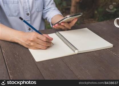 Hand woman write notebook and holding phone on wood table.