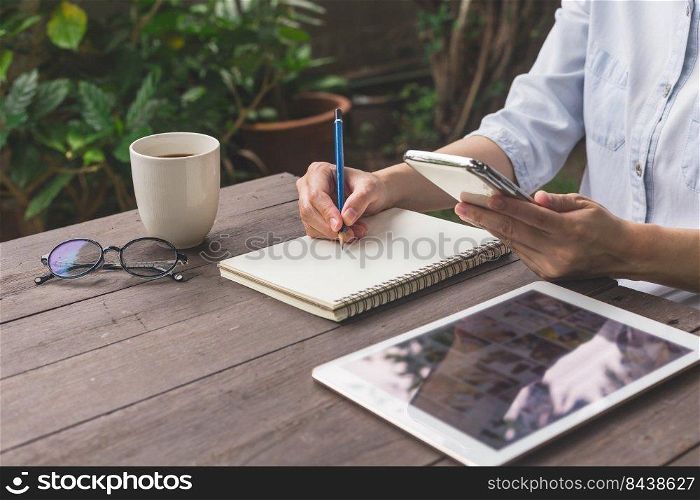 Hand woman write notebook and holding phone on wood table with cup coffee.
