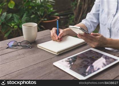 Hand woman write notebook and holding phone on wood table with cup coffee.