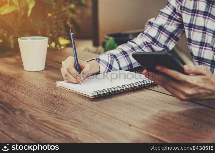 Hand woman writing notebook and holding phone on table in garden with vintage toned.