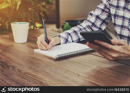 Hand woman writing notebook and holding phone on table in garden with vintage toned.