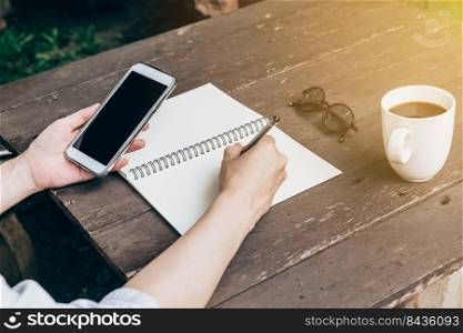 Hand woman writing notebook and holding phone on wood table backhround with vintage toned.