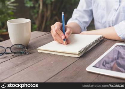 Hand woman writing notebook on wood table with cup coffe and tablet.