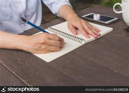Hand woman writing notebook on wood table with cup coffee and phone.