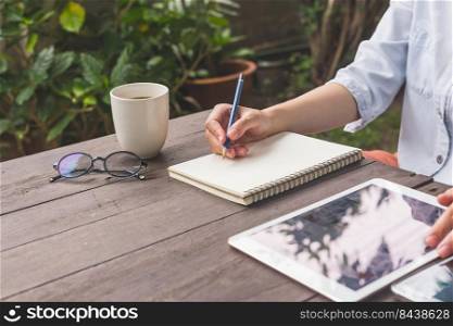 Hand woman writing notebook on wood table with cup coffee and tablet.