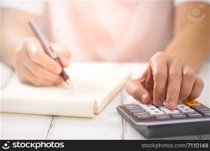 Hand writing and counting on calculator in office on wood desk about financial data analyzing, Choose focus point. In over light.