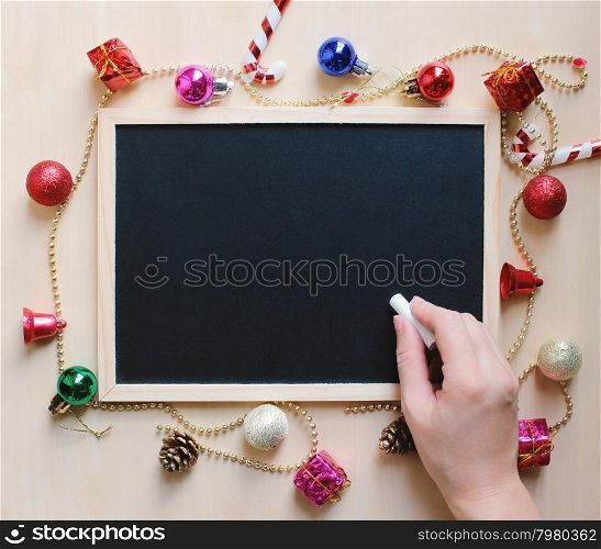 Hand writing with chalk on blank blackboard with christmas ornament