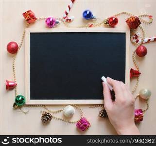 Hand writing with chalk on blank blackboard with christmas ornament