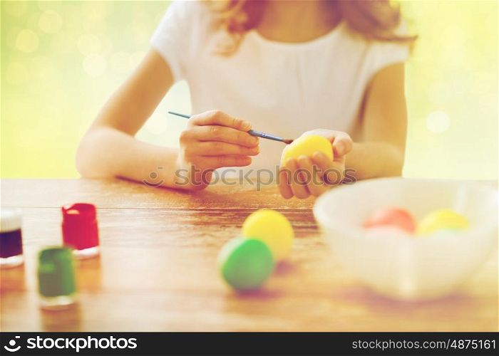 handcraft and people concept - close up of girl coloring easter eggs over green holidays lights background. close up of girl with brush coloring easter eggs