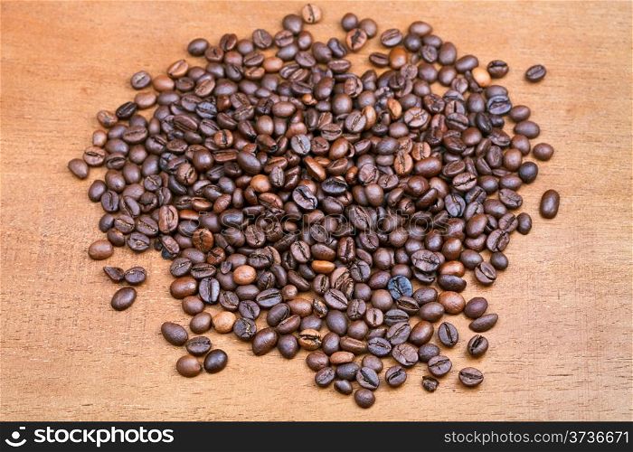handful of roasted coffee beans on wood plank close up