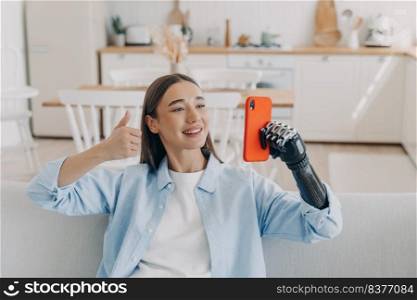Handicapped confident woman has video call on smartphone. Happy european girl is holding the phone with bionic artificial arm. Attractive handicapped woman at home. Equality and life quality concept.. Handicapped confident woman has video call on smartphone. Girl is holding phone with artificial arm.