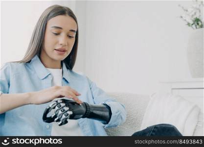 Handicapped girl is exploring her bionic arm and pressing buttons. Young european woman with cyber hand at home. Modern bionic prosthesis. Futuristic technology of artificial limbs.. Handicapped girl is exploring her bionic arm and pressing buttons. Futuristic technology.
