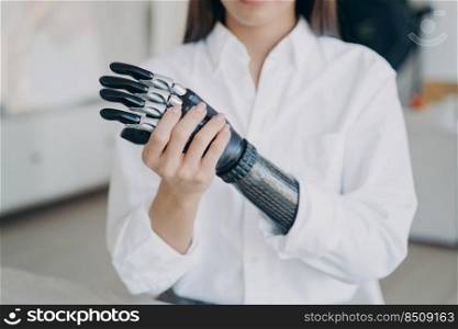 Handicapped young woman is assembling bionic arm with hand. Cyber sensor hand has processor chip and buttons. European girl adjusting contemporary electronic hand prosthesis at home.. Handicapped young woman is assembling bionic arm with hand. Girl is adjusting prosthesis.