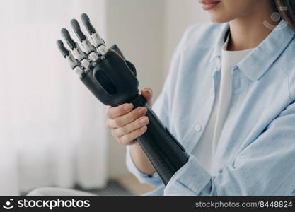 Handicapped young woman is disassembling bionic arm prosthesis. Cyber sensor hand has processor chip and buttons. Caucasian girl is&utee adjusting her electronic artificial arm at home.. Handicapped young woman is disassembling cyber sensor hand. Electronic artificial arm.