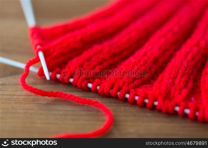 handicraft and needlework concept - close up of hand-knitted item with knitting needles on wood. hand-knitted item with knitting needles on wood
