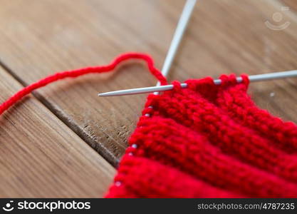 handicraft and needlework concept - close up of hand-knitted item with knitting needles on wood. hand-knitted item with knitting needles on wood