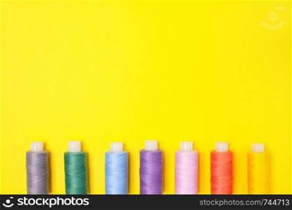 Handicraft background. Set of multicolored spools of thread on yellow background with copy space. Accessories for needlework, embroidery, sewing. Flat lay. Top view. Items are lined up at bottom edge.