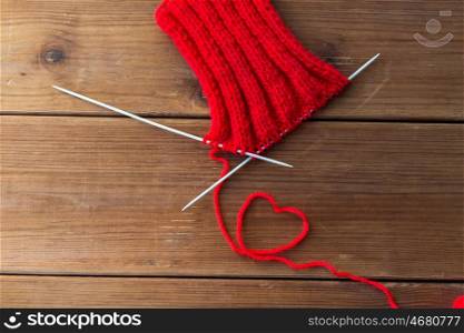 handicraft, love, valentines day and needlework concept - hand-knitted item with knitting needles and thread in heart shape on wood