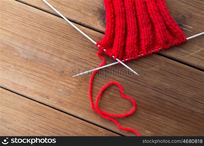 handicraft, love, valentines day and needlework concept - hand-knitted item with knitting needles and thread in heart shape on wood