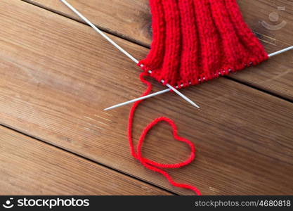 handicraft, love, valentines day and needlework concept - hand-knitted item with knitting needles and thread in heart shape on wood