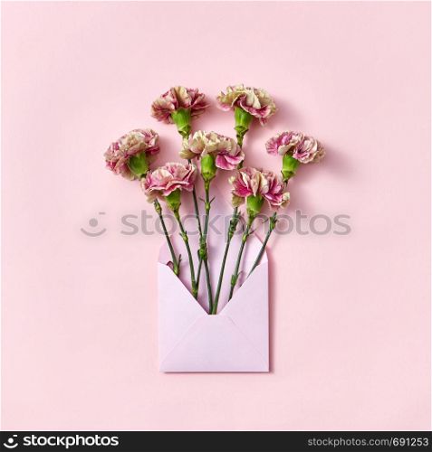 Handmade blank envelope with bouquet of carnations flowers on a pastel pink background, copy space. Top view. Congratulation card.. Carnation flowers in an envelope on a pastel pink background.