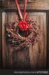 Handmade Christmas wreath hanging on wooden door with red ribbon and berries , front view
