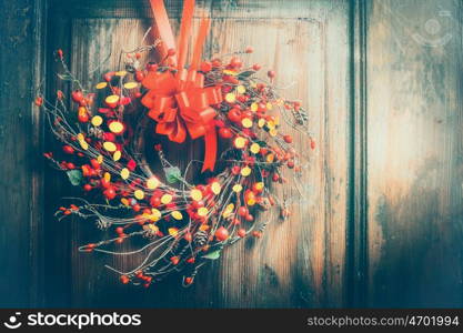 Handmade Christmas wreath hanging on wooden door with red ribbon , berries and bokeh lighting, front view, retro styled, place for text