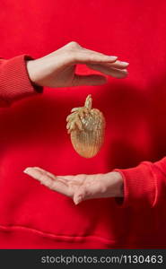 Handmade golden New Year decoration is hanging on woman&rsquo;s finger on the background of her red sweatshirt. Christmas greeting card.. Golden Christmas decoration in the hands.