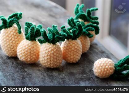 Handmade product from knit on grey wooden background, group of pineapples fruit in yellow with green leaf from amigurumi art for interior design