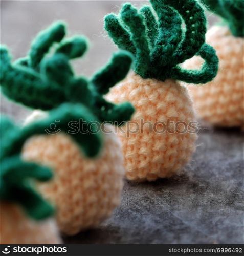 Handmade product from knit on grey wooden background, group of pineapples fruit in yellow with green leaf from amigurumi art for interior design