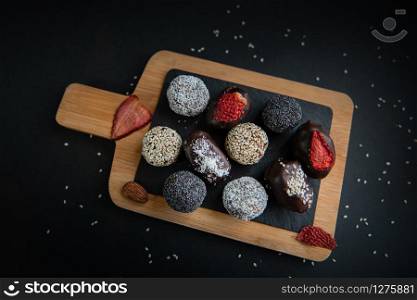 handmade sugar free and gluten free fruit and chocolate candies on a wooden board and black background. Top view of set handmade fruit and chocolate candies on a wooden board