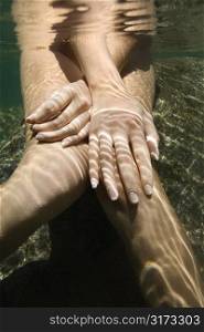 Hands and legs of Caucasian nude female sitting underwater.