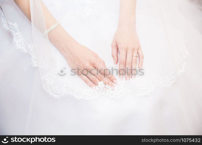Hands bride with a manicure, on the finger of the bride wedding ring, hands on the background of white lace dress covered with a veil in studio.. Hands bride with a manicure, on the finger of the bride wedding ring.