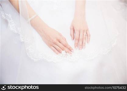 Hands bride with a manicure, on the finger of the bride wedding ring, hands on the background of white lace dress covered with a veil in studio.. Hands bride with a manicure, on the finger of the bride wedding ring.
