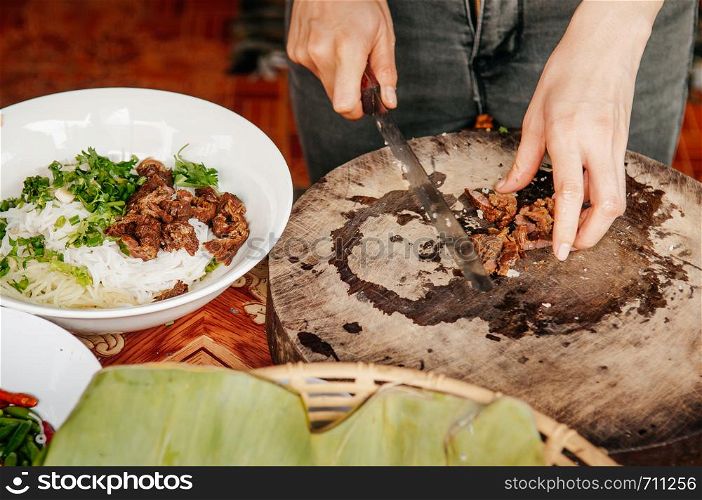 Hands chopping Asian style barbeque stewed pork for rice noodle